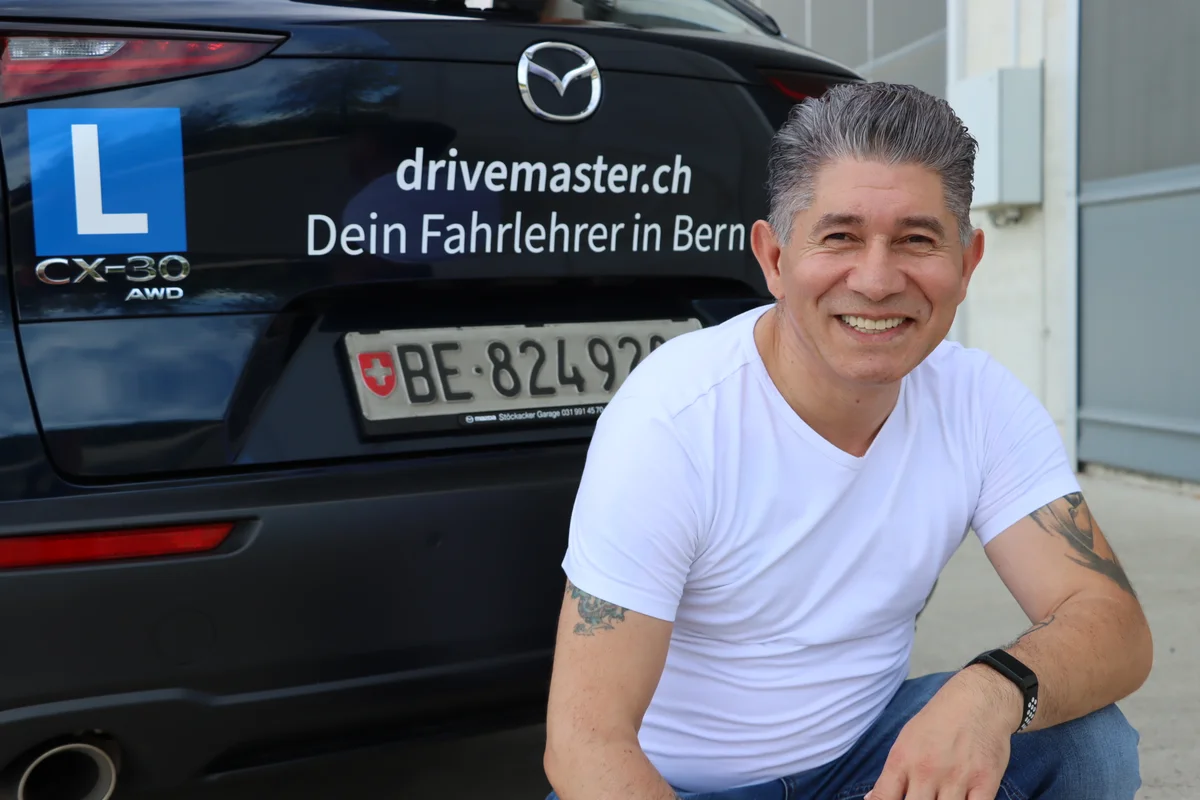 Mishel Memedovski - Dein geduldiger Fahrlehrer in Bern Mishel Memedovski - Fahrlehrer der Drivemaster Fahrschule Bern vor seinem Mazda CX-30 AWD Fahrschulauto mit L-Schild und Berner Kennzeichen